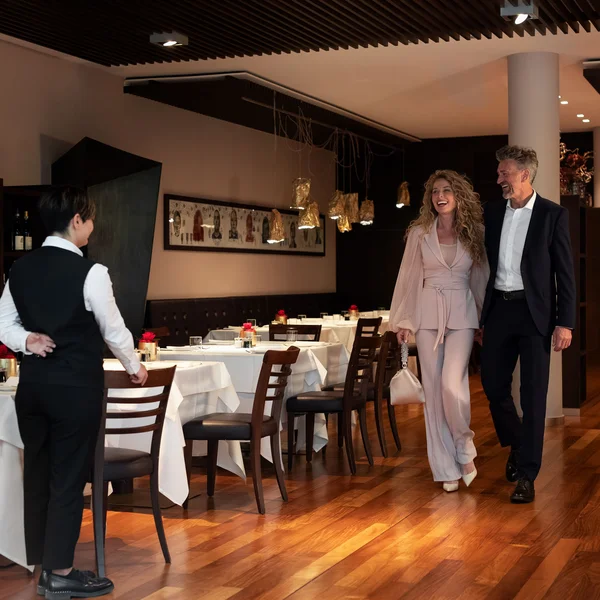Elegantes Paar wird von Kellner im modernen Restaurant begrüßt